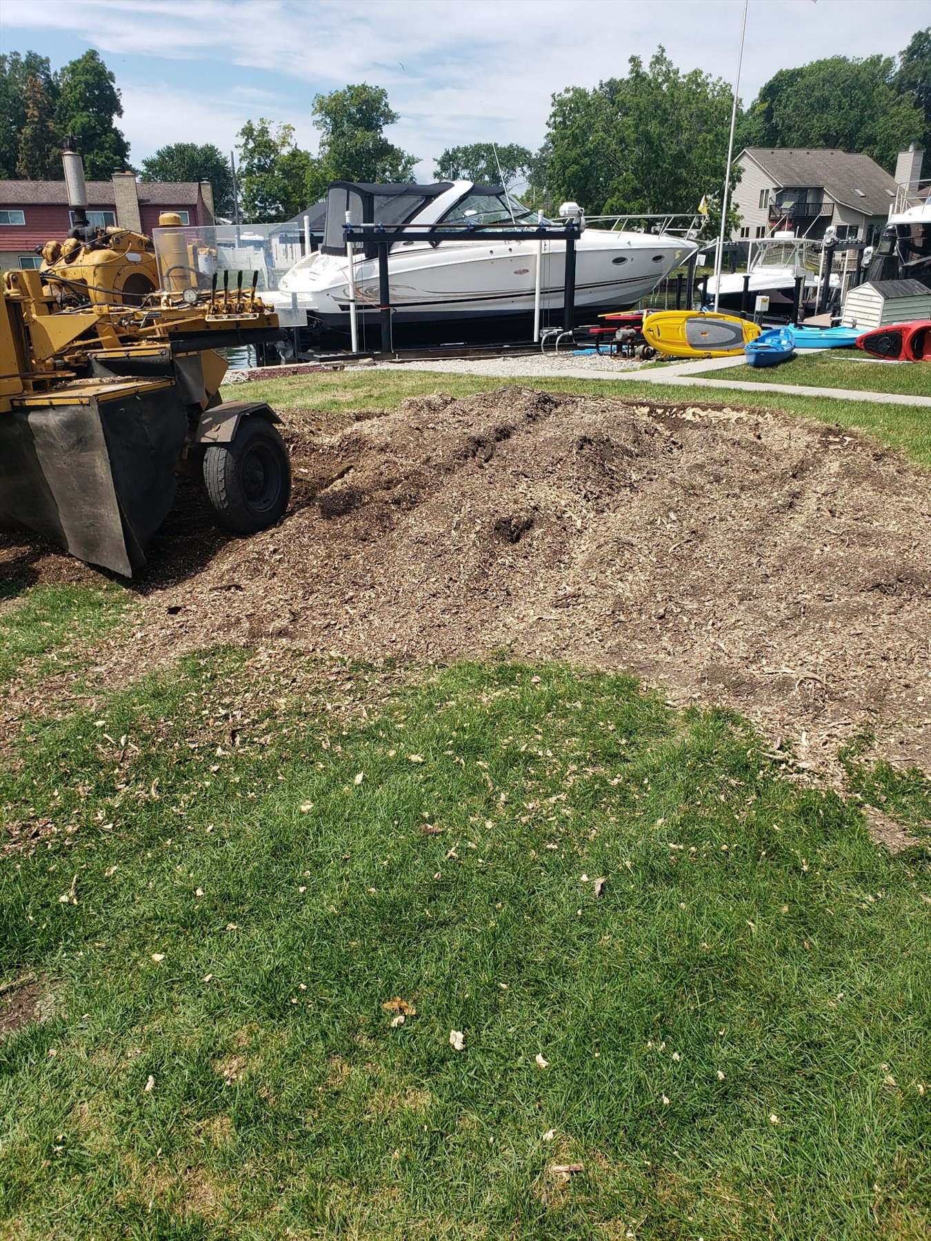 A stump grinder beside wood chips and the ground area after stump grinding at a waterfront property